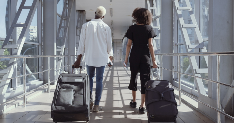 Back view of afro american couple walking together in airport going on vacation trip. Travel together. Carry backpack and suitcases. Attractive young woman and man with suitcases ready for traveling Royalty-Free Stock Footage #1060791481
