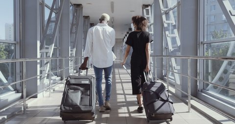Back view of afro american couple walking together in airport going on vacation trip. Travel together. Carry backpack and suitcases. Attractive young woman and man with suitcases ready for traveling