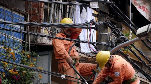 Hanoi / Vietnam - 04 12 2019: Two utility electrician workers fix a broken voltage cable line high on a pole on the street