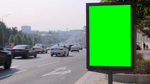 Green screen billboard located on a busy street. Cars move in a stream. Working day morning. In the foreground there is an arrow indicating the direction of the vehicles.