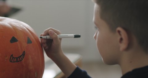 Close-up of kid drawing halloween holiday decoration on punpkin . Social campaign for pandemic coronavirus covid-19 prevention.