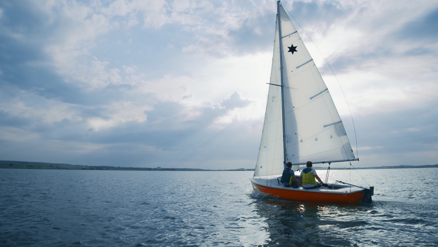 Sailing yacht moving across wide beautiful lake in sunny morning. Sunrise at seaside. Yacht tour. Sialing activity. Sailors men. Landscape, natural concept.