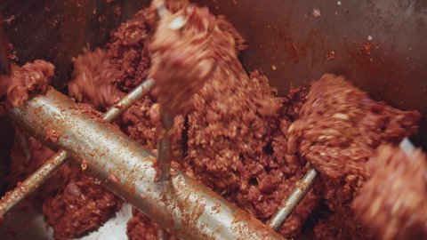 Process of sausage manufacturing. Delicious raw minced meat rotating in industrial large grinder mixer with red hot spices. Meat factory concept.