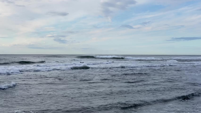 Two surfers glide on the waves of the Pacific Ocean. Khalaktyrsky beach, Kamchatka peninsula. Black volcanic sand beach.