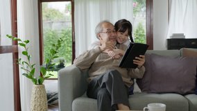 Candid of old senior asian grandparent play and watch with kid grandchildren with technology on computer tablet at home in bonding relationship in family. Young girl hug older man from back. - Powered by Shutterstock - Get 15% off with code: PIKWIZARD15