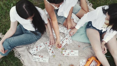 Interesting hazardous pastime. Friends women enjoying picnic on green lawn in park playing lotto games