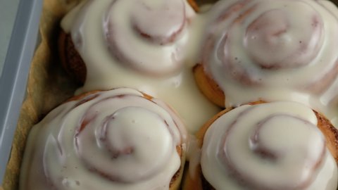 Pouring frosting on Freshly baked cinnamon rolls or Cinnabon close up. Sweet cream cheese frosting pouring on cinnamon rolls. Production of cinnamon rolls. Bakery products. Appetizing cinnamon buns