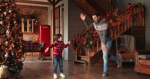 Dad dancing with little son enjoy Christmas together at ornate house hall with bright illuminated lights and xmas tree. Funny activity with child, hobby, New Year winter holidays celebrations concept