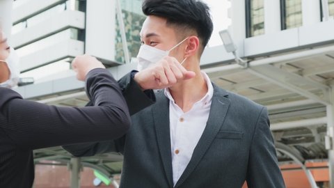 Asian business people wearing protective face mask outside in city due to covid pandemic crisis. Male and female office workers making elbow touch instead of handshake to avoid coronavirus infection.