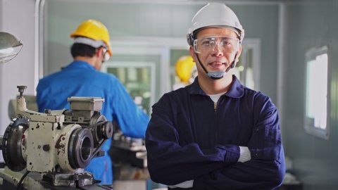 Asian mechanical workers working on milling machine. The technicians wearing protective glasses and helmet when operating the machine for safety precaution. Portrait of man crossed arm looks at camera