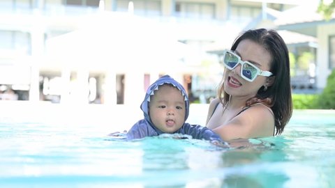 Asian cheerful mother and little son enjoying swimming in a swimming pool