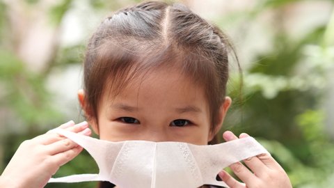 Slow motion happy litle children asia girl wearing protective medical face mask in public park background. Practicing social distancing, Coranavirus COVID-19. Health Care and Virus Protection Concept.