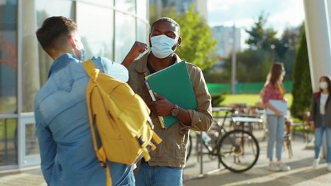 Quarantine. Two multi-race students wearing face masks meeting with elbows greeting talking outdoors. Social distance. Virus protection. Coronavirus. Lockdown.