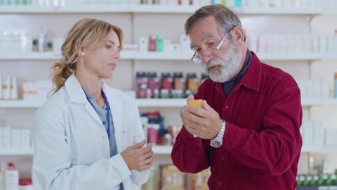 Slow motion woman pharmacist serving old man customer in a drugstore. Conversation pharmaceutical client. Seller commercial health care buyer uniform. Close up