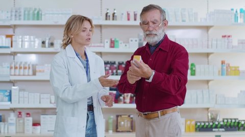 In pharmacy woman pharmacist serving old man customer drugstore. Conversation pharmaceutical client. Seller commercial health care buyer uniform. Slow motion