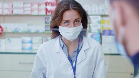 Professional woman pharmaceutist in face mask consulting sick caucasian patient making drugs recommendations prescription selling medicine in apothecary. Medicare. Influenza.
