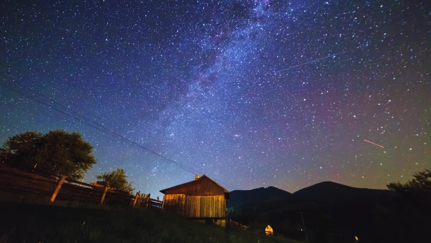 The Milky Way galaxy rotating in the night sky over the high mountain village with a rising moon in the middle of the night. Star trails timelapse, 4K