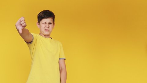 Dislike gesture. Disgusted kid. Ugh gross. Bad idea. Skeptic displeased young boy denying offer with thumbs down isolated on yellow copy space background.
