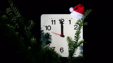 Clock in branches of New Year's fir on black background. Second hand moves in circle of mechanical clock and show Twelve o'clock at  Midnight and eve of Christmas. Holiday concept, time lapse, closeup