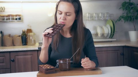 Young woman eating chocolate paste in the kitchen in the evening. The girl feels a sense of pleasure eating a spoon of chocolate from a jar
