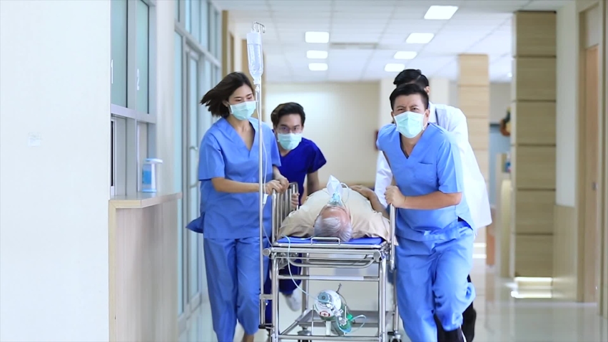 Group of Asian doctors and nurses team wearing face mask, push emergency stretcher, transport senior patient Through Hospital Corridors. Medical rescue team in a Hurry Move Patient operation concept.