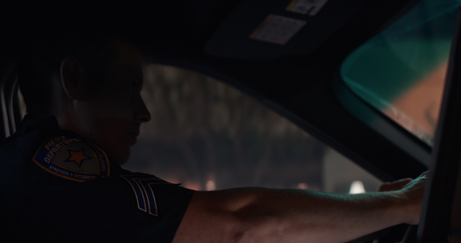 CU Portrait of police officer talking on CB radio while driving in a vehicle through city streets at night. Shot on RED Dragon with 2x Anamorphic lens Royalty-Free Stock Footage #1060829704