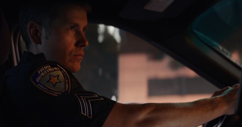CU Portrait of police officer talking on CB radio while driving in a vehicle through city streets at night. Shot on RED Dragon with 2x Anamorphic lens