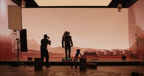 Behind the scenes shot of virtual production stage with huge LED screens, cinematorgapher shooting Mars scene. Future of movie production