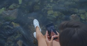 A woman sits on a wooden pier and takes pictures of her feet against the background of the sea. Close-up on female legs and the sea. View from above. High quality 4k footage