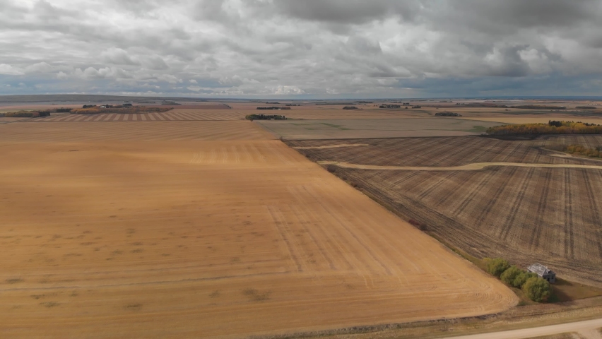 Drone moving forward high above a vast prairie landscape of harvested autumn farm fields.  The land is very flat, and the sky is full of stormy looking gray clouds.