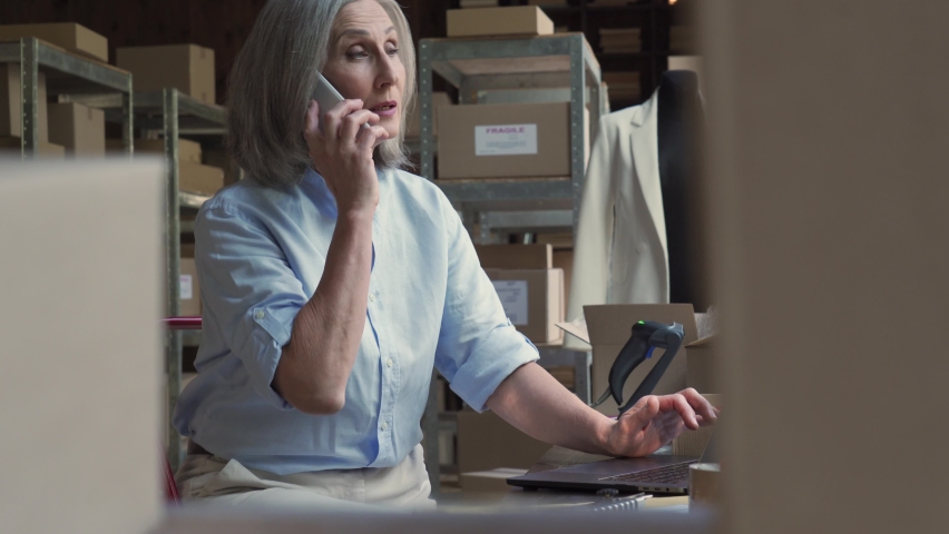 Mature older woman seller entrepreneur, clothing store online dropshipping small business owner talking with customer confirming ecommerce parcel order on laptop in postal delivery shipping warehouse. | Shutterstock HD Video #1060830646