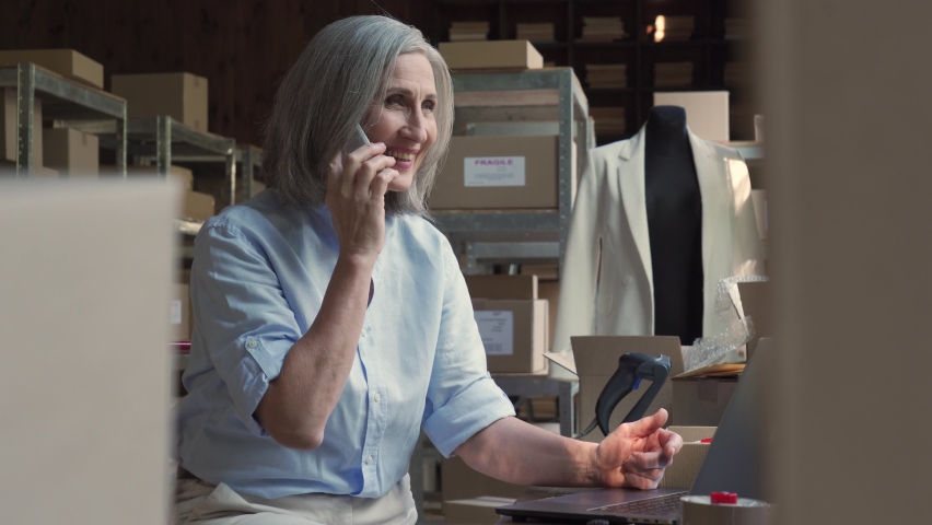 Mature older woman seller entrepreneur, clothing store online dropshipping small business owner talking with customer confirming ecommerce parcel order on laptop in postal delivery shipping warehouse. Royalty-Free Stock Footage #1060830646