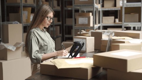 Female warehouse worker online store owner using laptop at work preparing parcel boxes checking ecommerce shipping online retail e commerce store order fulfillment in dropship delivery post office.