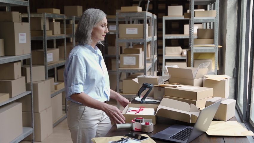 Middle aged older female online store small business owner, warehouse worker, merchant packing package shipping ecommerce retail order in box preparing delivery parcel on table. Dropshipping service. Royalty-Free Stock Footage #1060830667