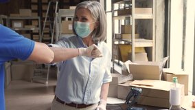 Female warehouse worker manager wearing face mask greeting male courier deliverer giving elbow bump taking shipping parcels boxes for delivery. Covid 19 healthcare protection social distance at work. - Powered by Shutterstock - Get 15% off with code: PIKWIZARD15