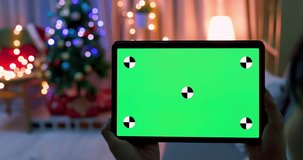asian woman watch green screen digital tablet while lying on couch with christmas tree and decoration at home