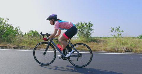 Side view of asian young woman wearing helmet is riding a bicycle on the road concentratedly