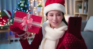 asian young woman wearing christmas clothes has video chat on smart phone and shows present box to her friend