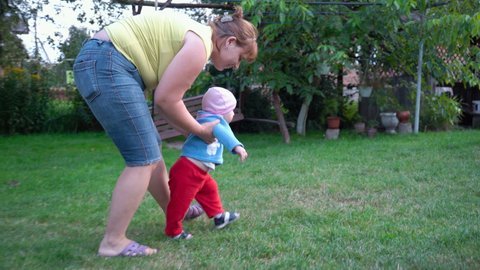 mother teaches baby to walk,the baby learns to walk in the yard with his mother