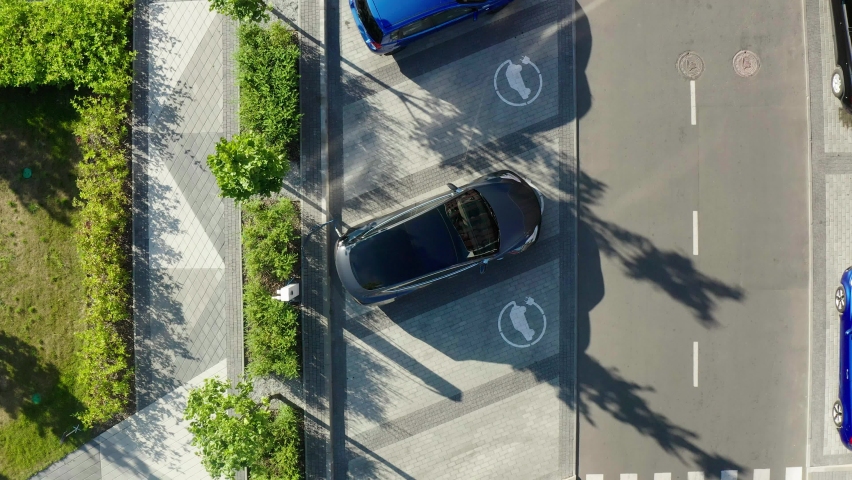 Aerial view of a white electric vehicle driving. 4K aerial overhead view on white electric vehicle parking at the charging station. Royalty-Free Stock Footage #1060840168