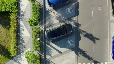 Aerial view of a white electric vehicle driving. 4K aerial overhead view on white electric vehicle parking at the charging station.