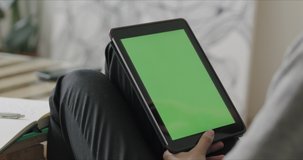 View over head on of caucasian woman holding tablet computer with green screen while watching something and working from home. Chroma key. 4k video footage slow motion
