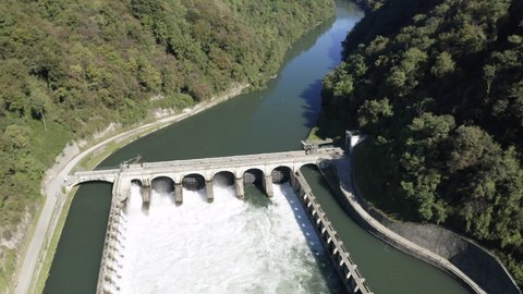 Aerial view of an historic hydroelectric power plant located on a river bank, which exploits the difference in height created by the dam on the Adda river, Italy