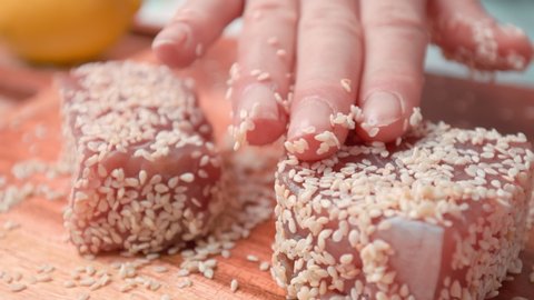 Close-up of woman's hands Coating raw tuna in sesame seeds in 4K. Concept of marinating/preparing yellowfin tuna in seeds for frying. Cooking Seared tuna step by step.