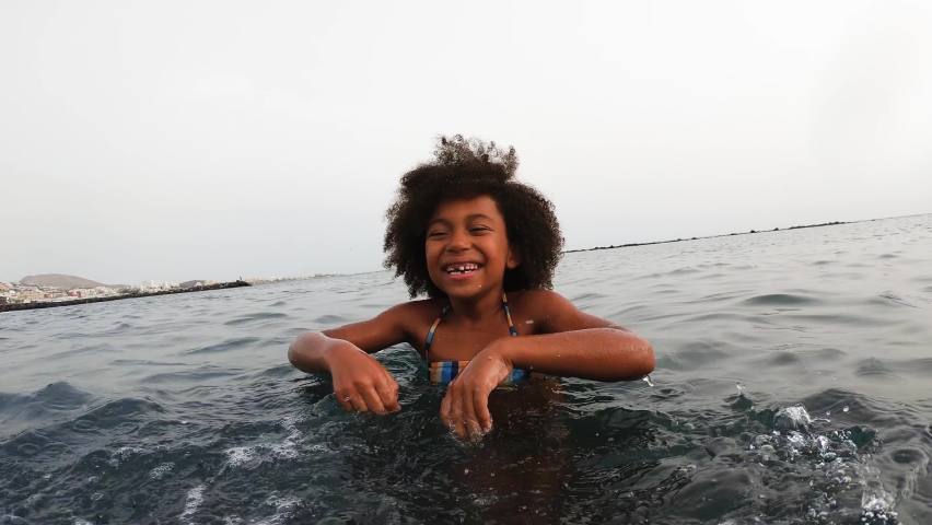 Afro child having fun throwing sea water in front of camera during vacation time | Shutterstock HD Video #1060851712