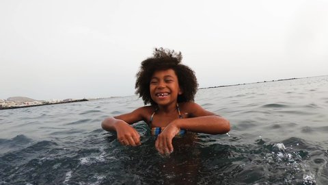 Afro child having fun throwing sea water in front of camera during vacation time