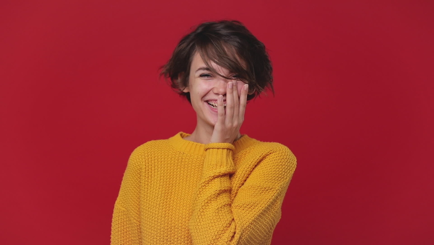 Young funny woman 20s in yellow sweater posing isolated on red background in studio. People sincere emotions in cinema lifestyle concept. Looking camera cheerful laughing smile watching comedy movie Royalty-Free Stock Footage #1060853491