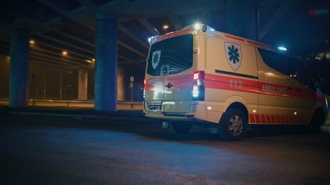 Ambulance Vehicle with Working Strobe Lights and Signal with Emergency Care Assistants Arrived on the Scene of a Traffic Accident on a Street at Night. Paramedics Team React to an Emergency Call.