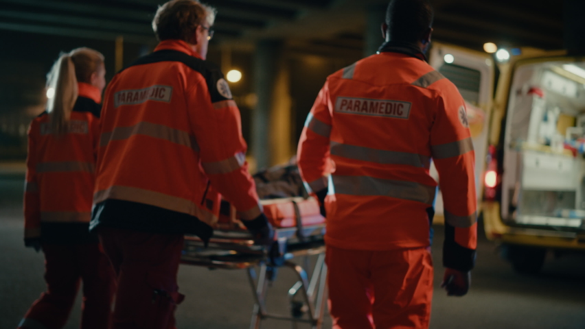 Team of EMS Paramedics React Quick to Provide Medical Help to Injured Patient and Get Him in Ambulance on a Stretcher. Emergency Care Assistants Arrived on the Scene of a Traffic Accident on a Street. Royalty-Free Stock Footage #1060859443