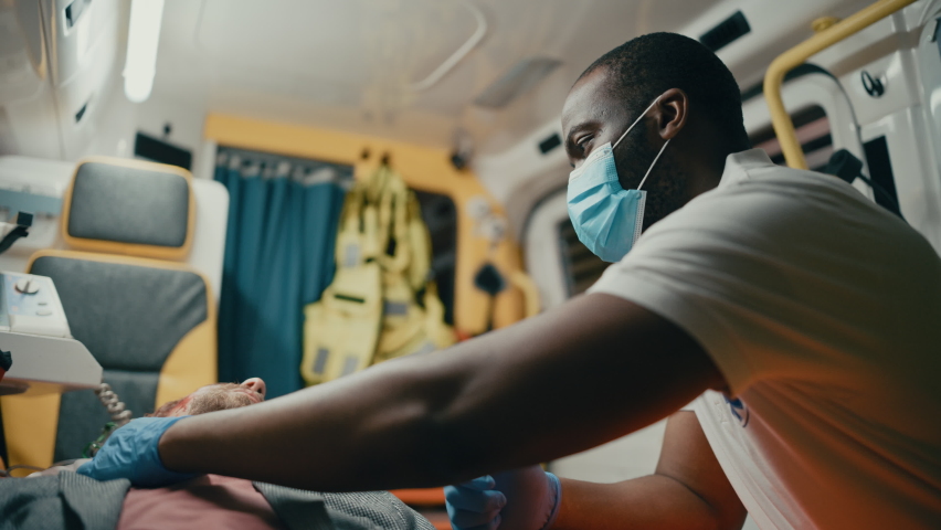 EMS Paramedic Wear Face Mask on the Ambulance Ride to Healthcare Hospital with Injured Patient. Emergency Care Assistant Checking Up and Using Flashlight on a Sick Young Man. Royalty-Free Stock Footage #1060859500